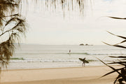 Pastel morning at Byron Bay, a longboarder crossing warm sand as a small wave peels behind, a surf wall print.