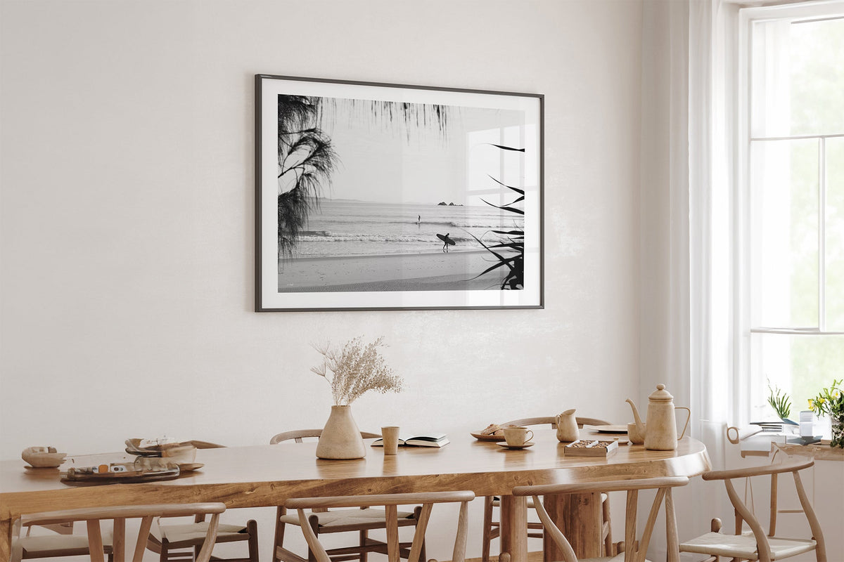 Byron Bay black and white surf print shown framed in black above an oak table.