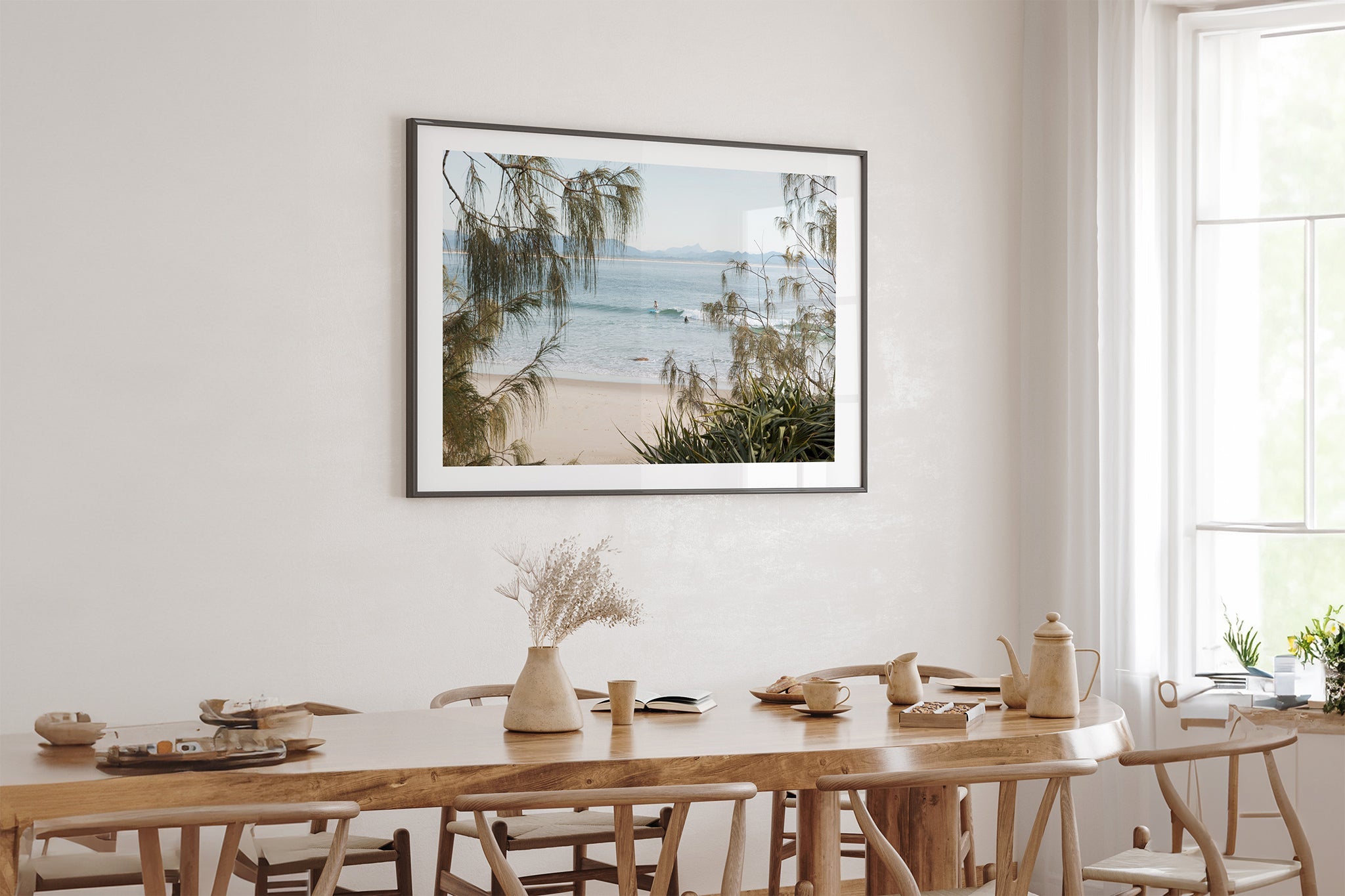Byron Bay coastal print shown framed in black above an oak table.