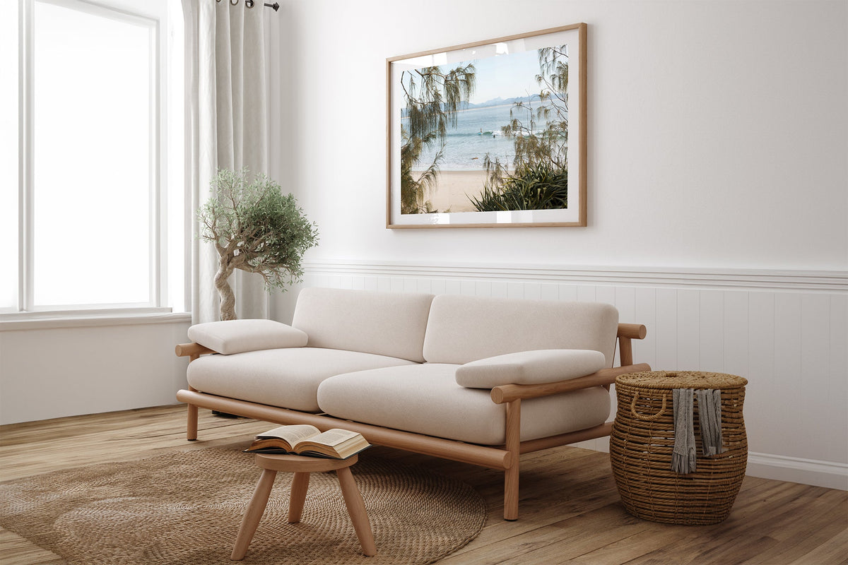 Byron Bay coastal print shown framed in oak above a linen couch.