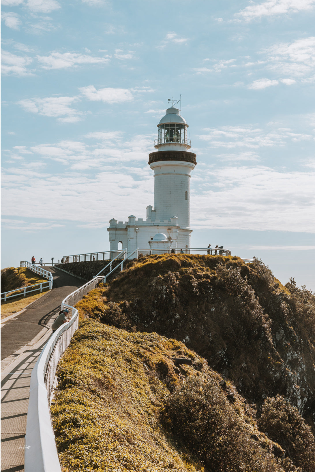 The white Cape Byron Lighthouse on a green headland at Byron Bay, a path curving up to it under soft cloud, a coastal wall print.