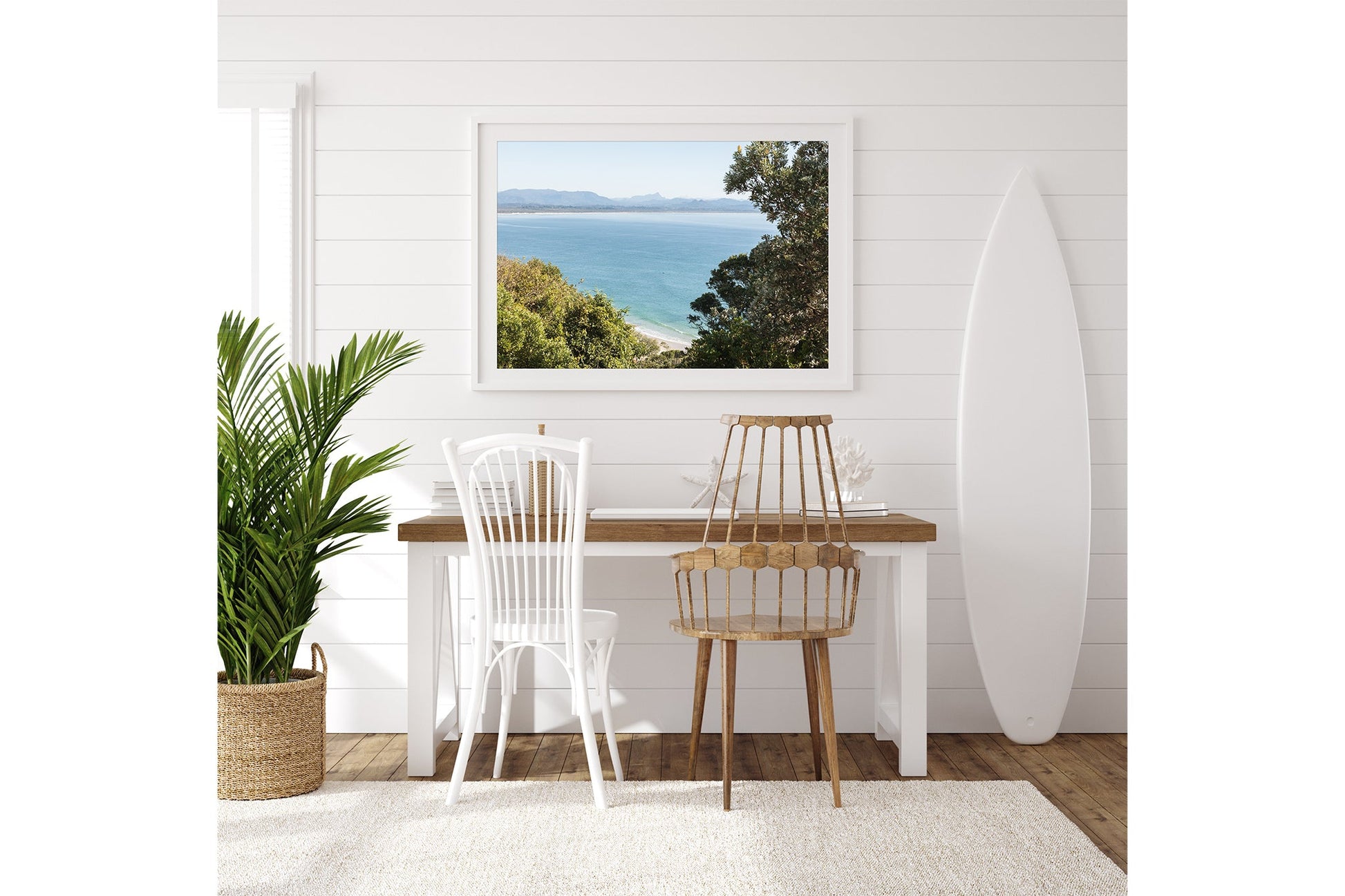 Byron Bay lookout print shown framed in white beside a surfboard in a coastal room.