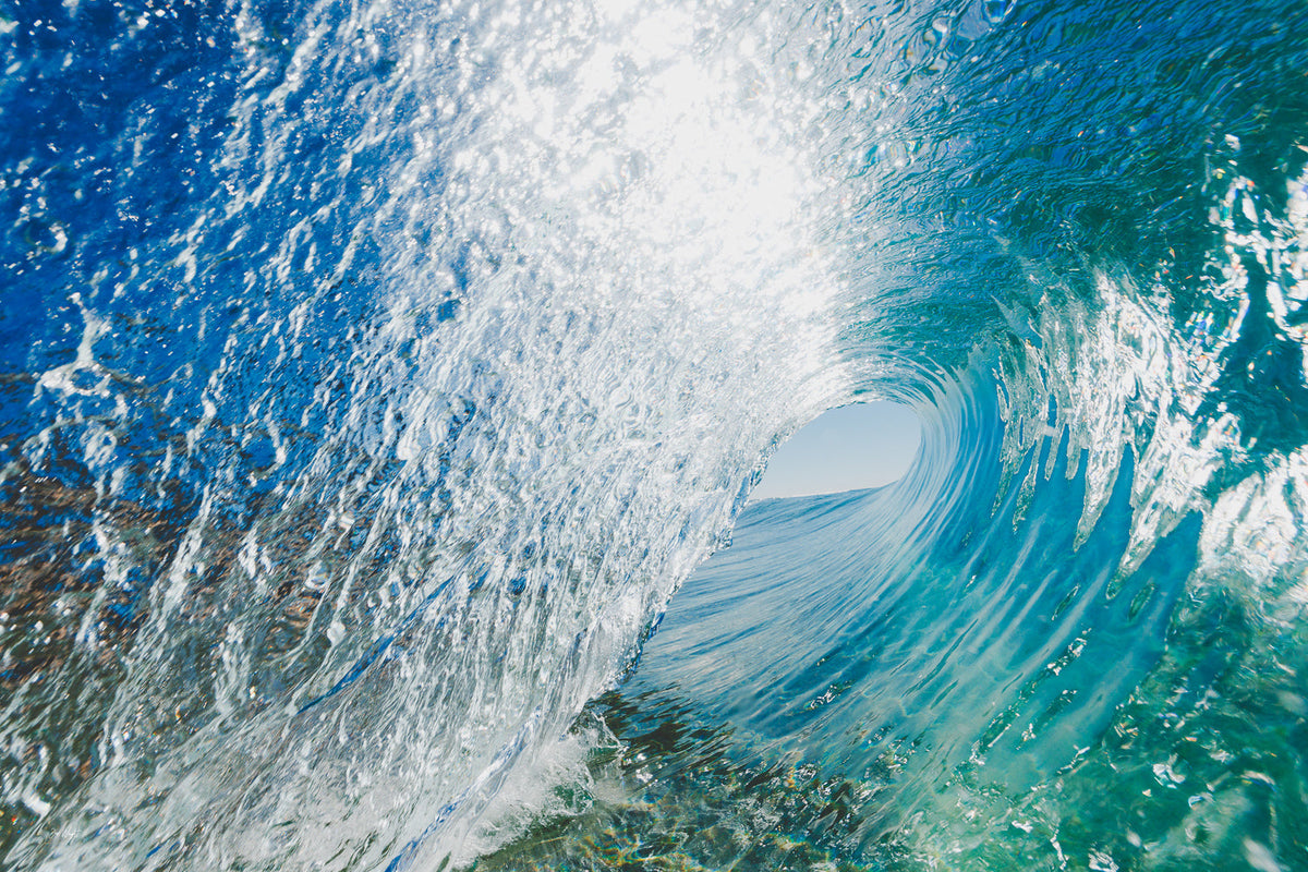 Inside a barrelling wave, streaks of white spray over deep blue and teal water curling toward a small opening of sky, an ocean wall print.