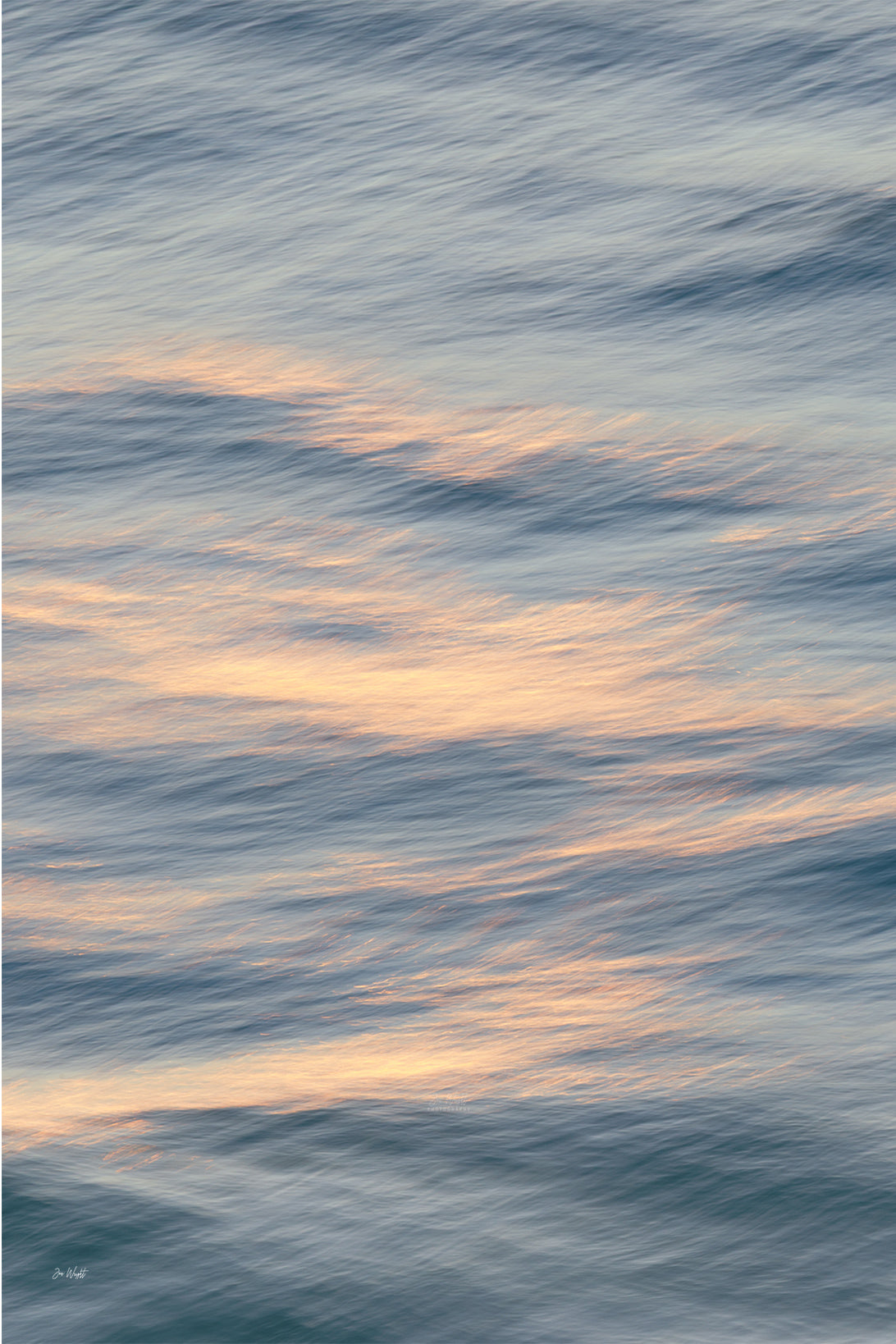 Soft peach and cream light drifting across grey blue rippled water, a gentle slow shutter abstract wall print.