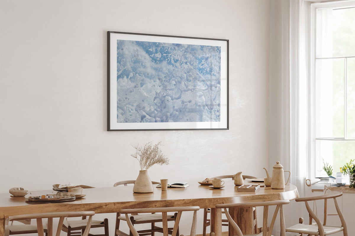 Frozen Splash print shown framed in black above an oak table.