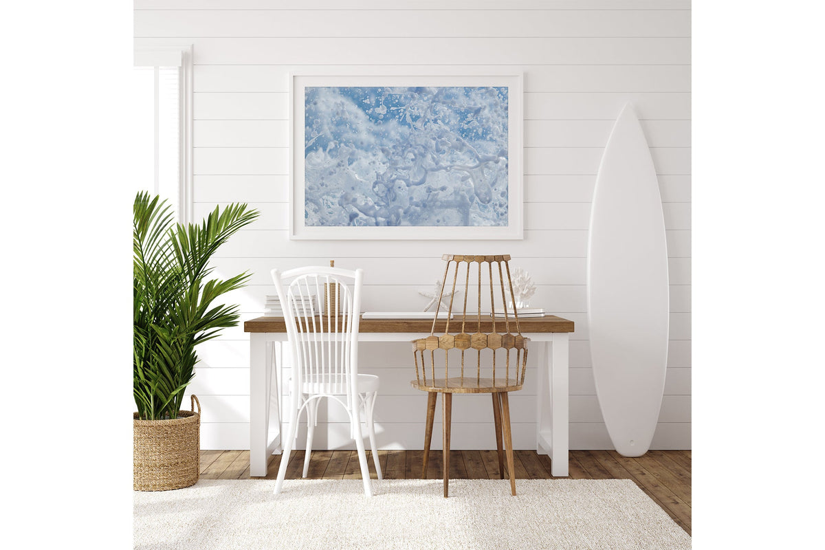 Frozen Splash print shown framed in white on a white shiplap wall with a surfboard leaning beside a desk.