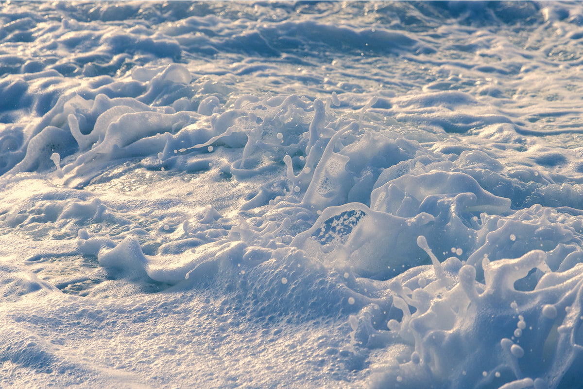 Sculpted white sea foam with cool blue shadows and a touch of warm gold light on the left, an abstract ocean wall print.