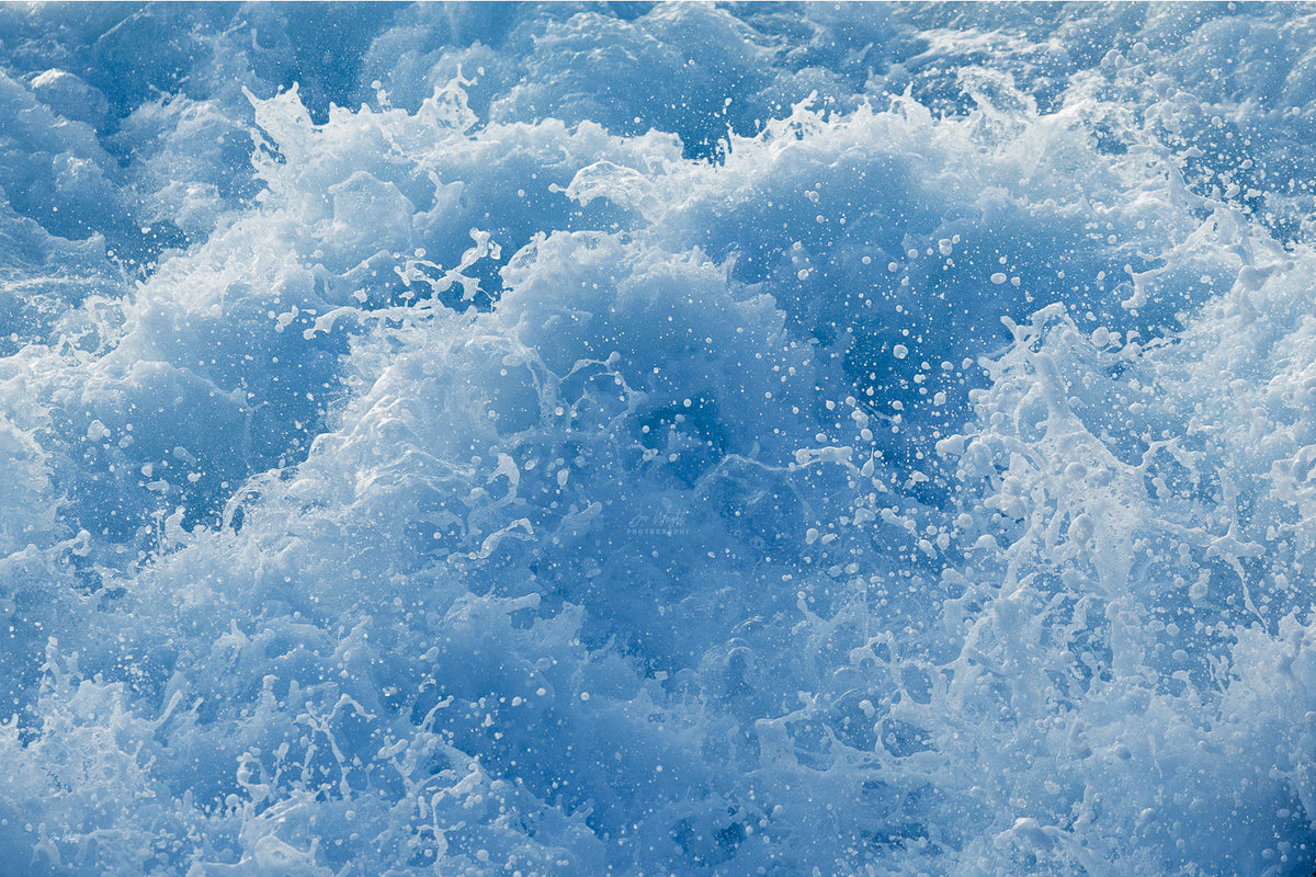 Churning cobalt blue water with bright white spray and droplets thrown in every direction, an ocean wall print.