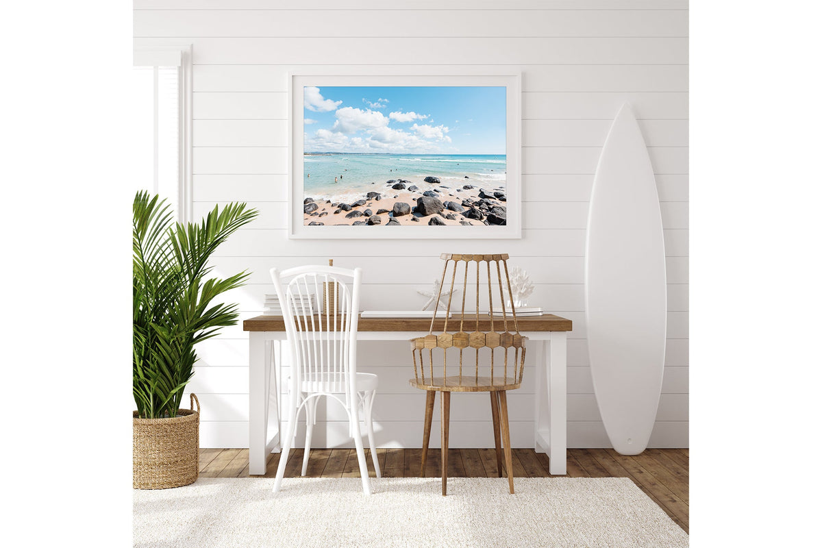 Rock Pool Shallows print shown framed in white on a white shiplap wall with a surfboard leaning beside a desk.