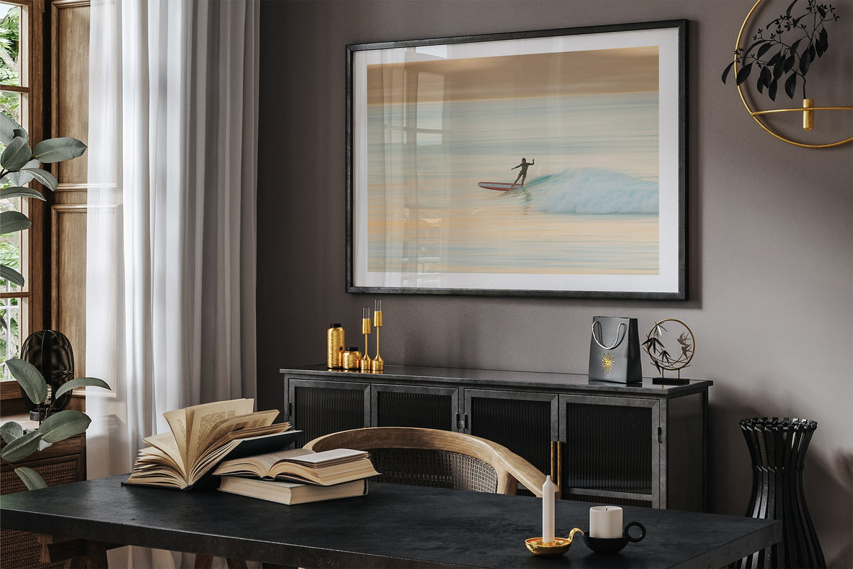 Longboard surfer print shown framed in black on a dark room wall.