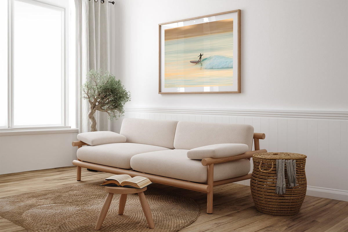 Longboard surfer print shown framed in oak above a couch.