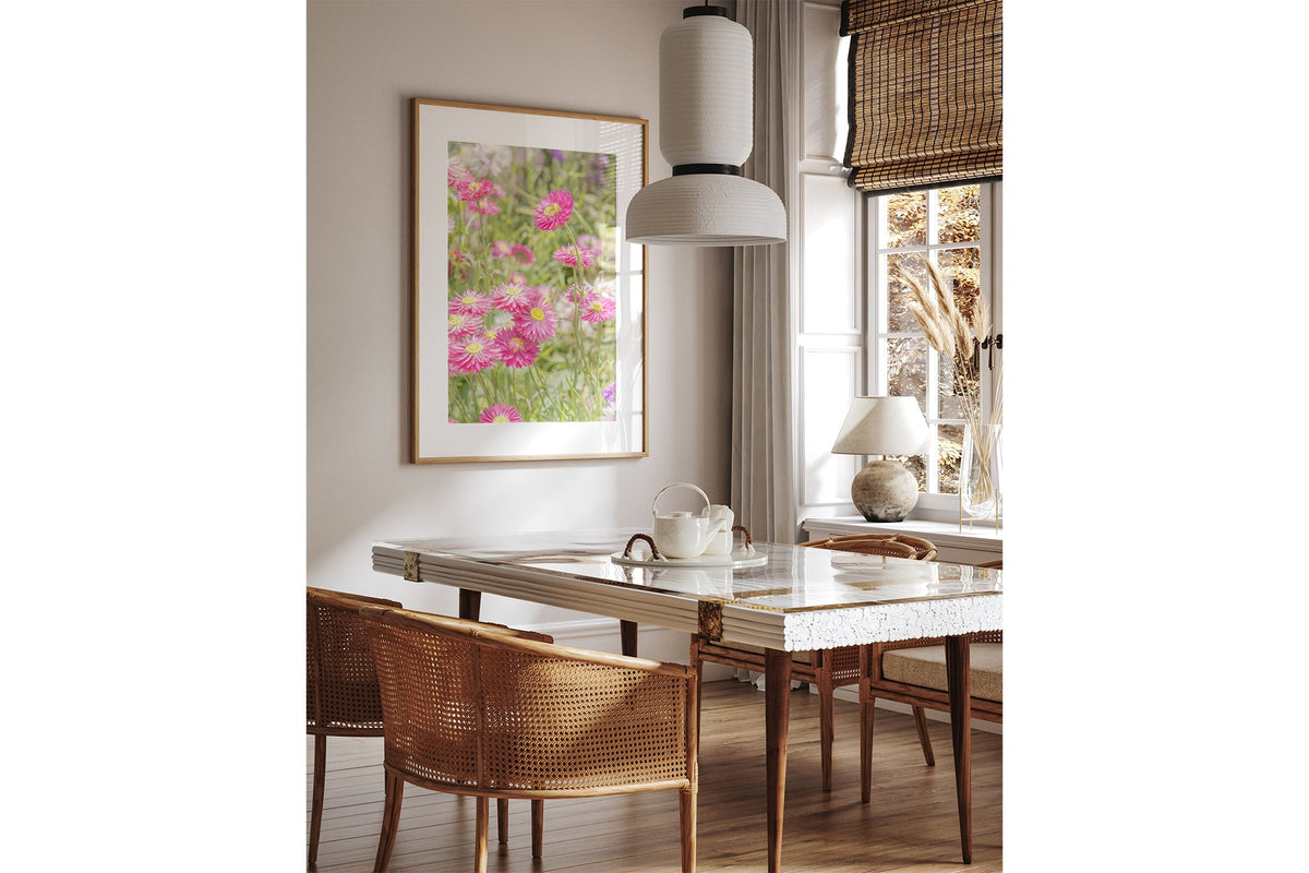 Pink strawflower print shown framed in oak above a dining table.