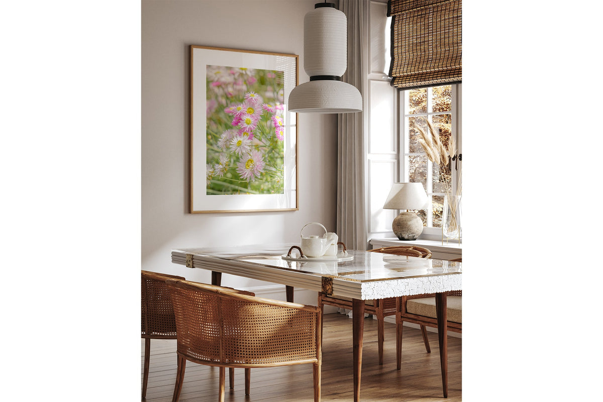 Blush strawflower print shown framed in oak above a dining table.