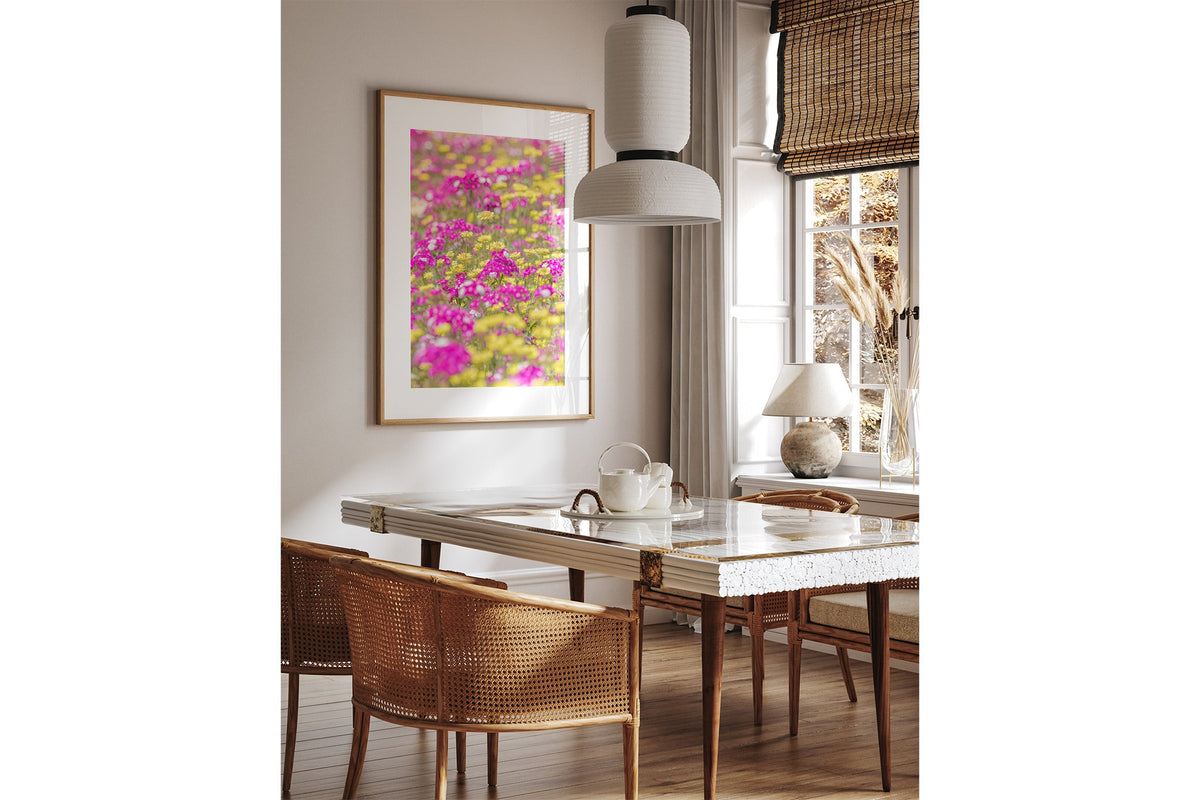 Pink and yellow meadow print shown framed in oak above a dining table.