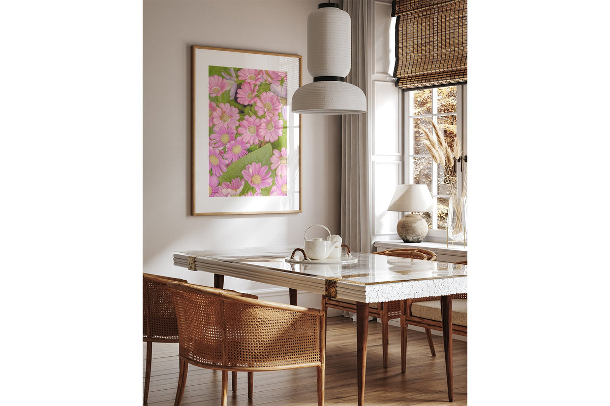 Pink daisy print shown framed in oak above a dining table.