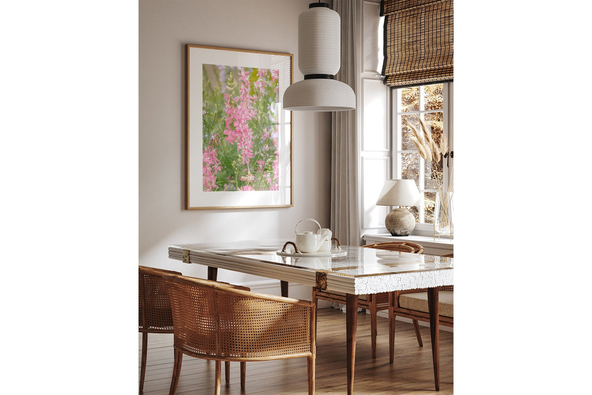 Pink larkspur print shown framed in oak above a dining table.