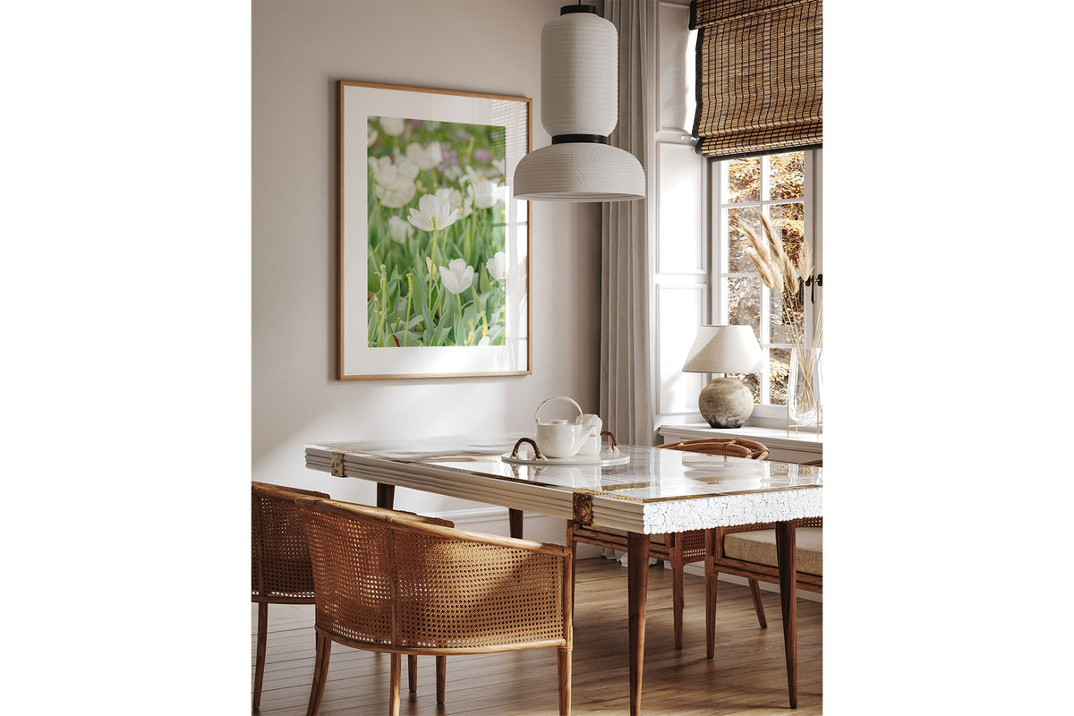 White tulip print shown framed in oak above a dining table.