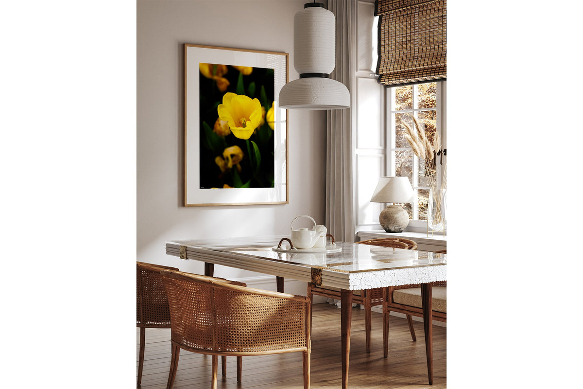 Yellow tulip print shown framed in oak above a dining table.