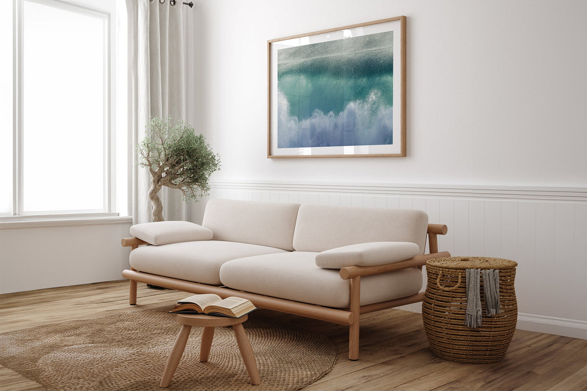 Aqua wave print shown framed in oak above a linen couch.