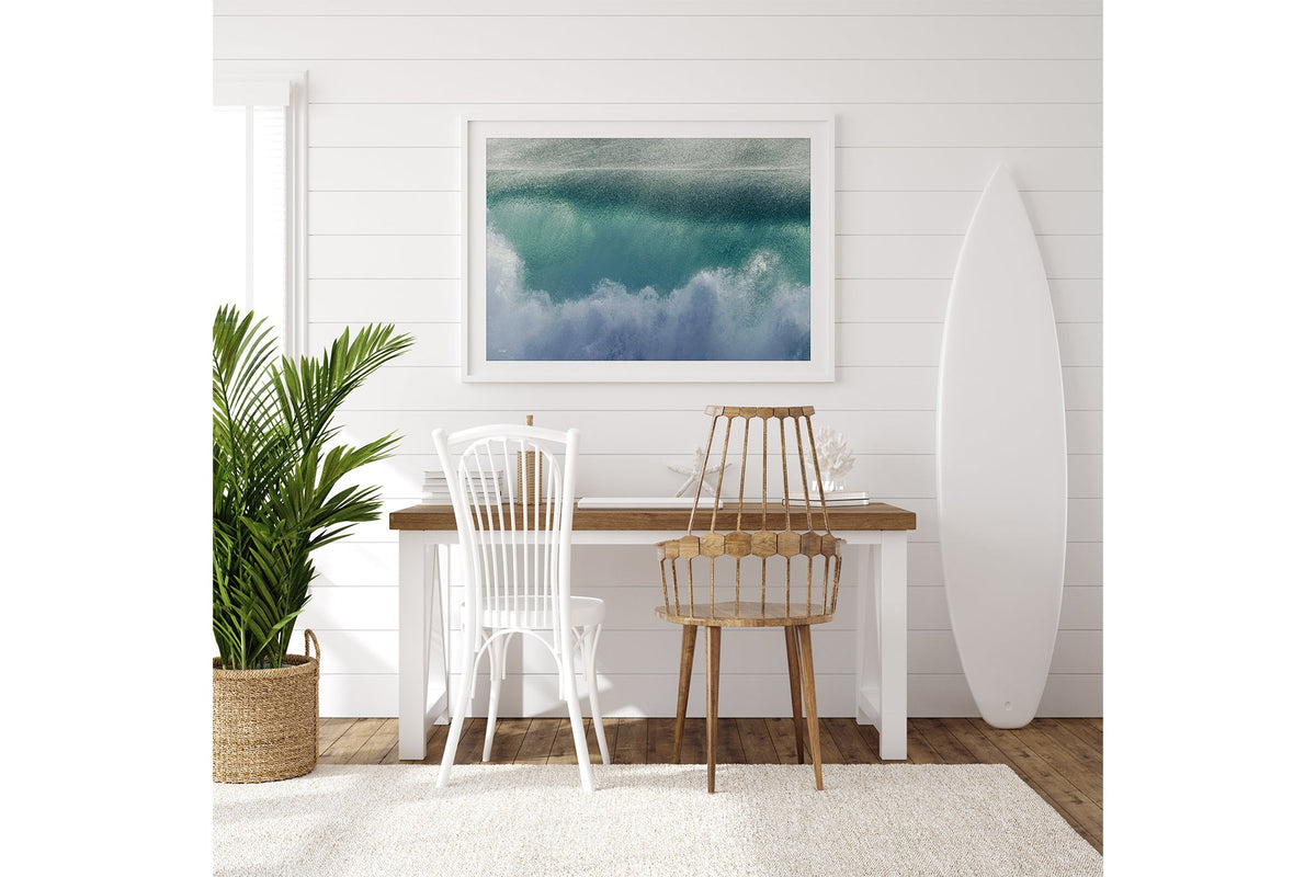 Aqua wave print shown framed in white on a white shiplap wall beside a desk.