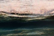 A band of rose pink foam across the top of a dark teal wave face with warm gold glints, an abstract ocean wall print.