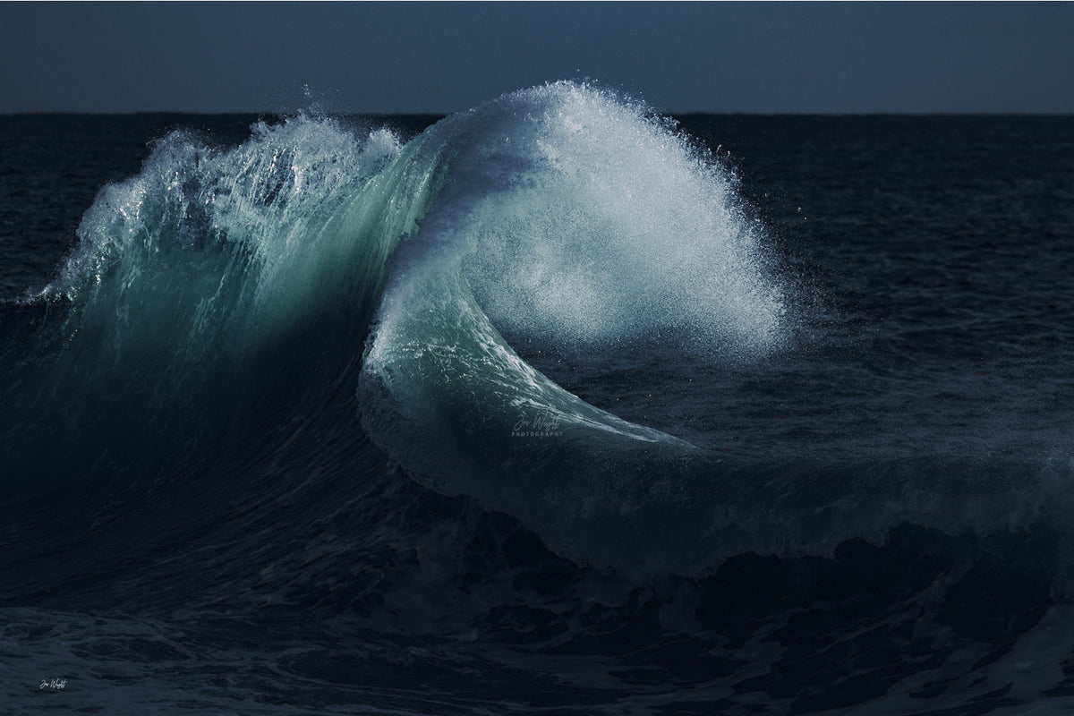 A teal and green wave curling over with a plume of white spray against near black navy water and sky, a moody ocean wall print.