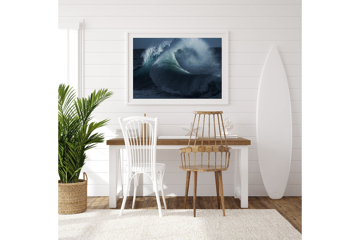 Rising Surge print shown framed in white on a white shiplap wall with a surfboard leaning beside a desk.