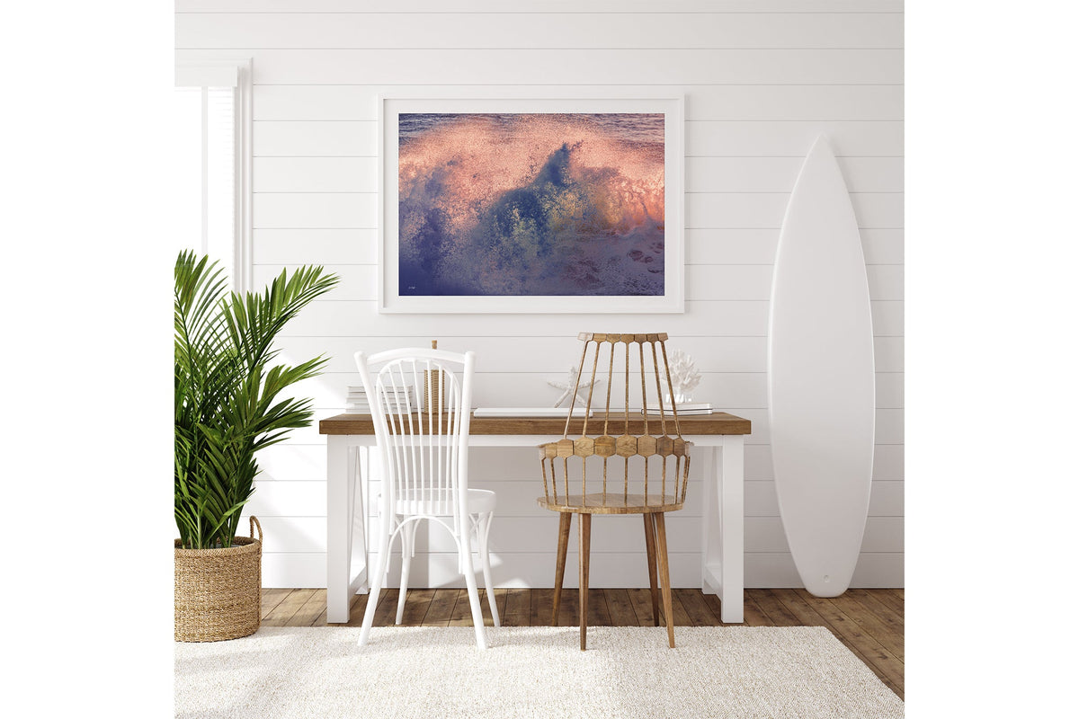 Dusk Burst print shown framed in white on a white shiplap wall with a surfboard leaning beside a desk.