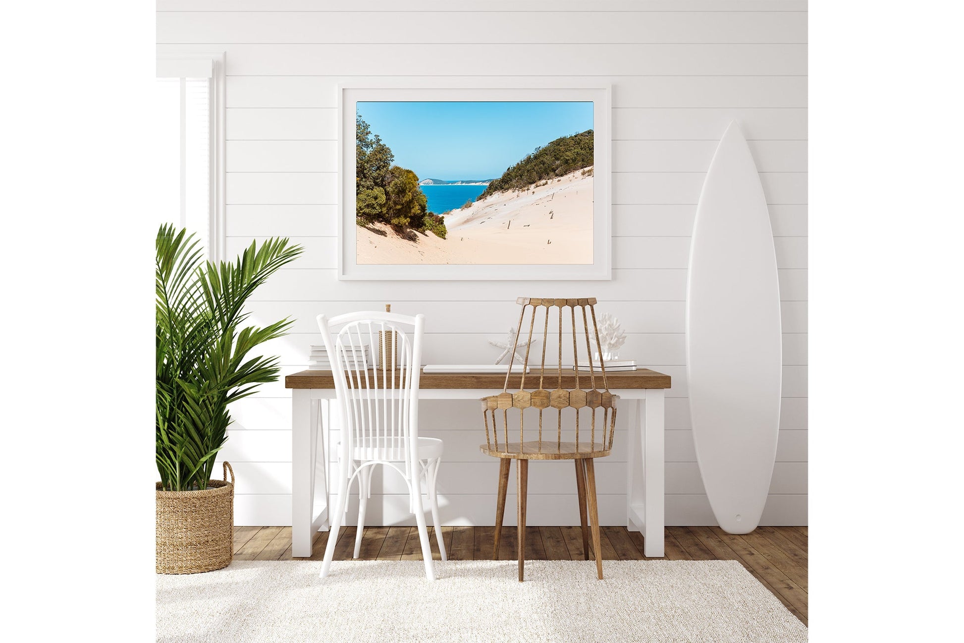 Rainbow Beach dune print shown framed in white above a desk beside a surfboard.