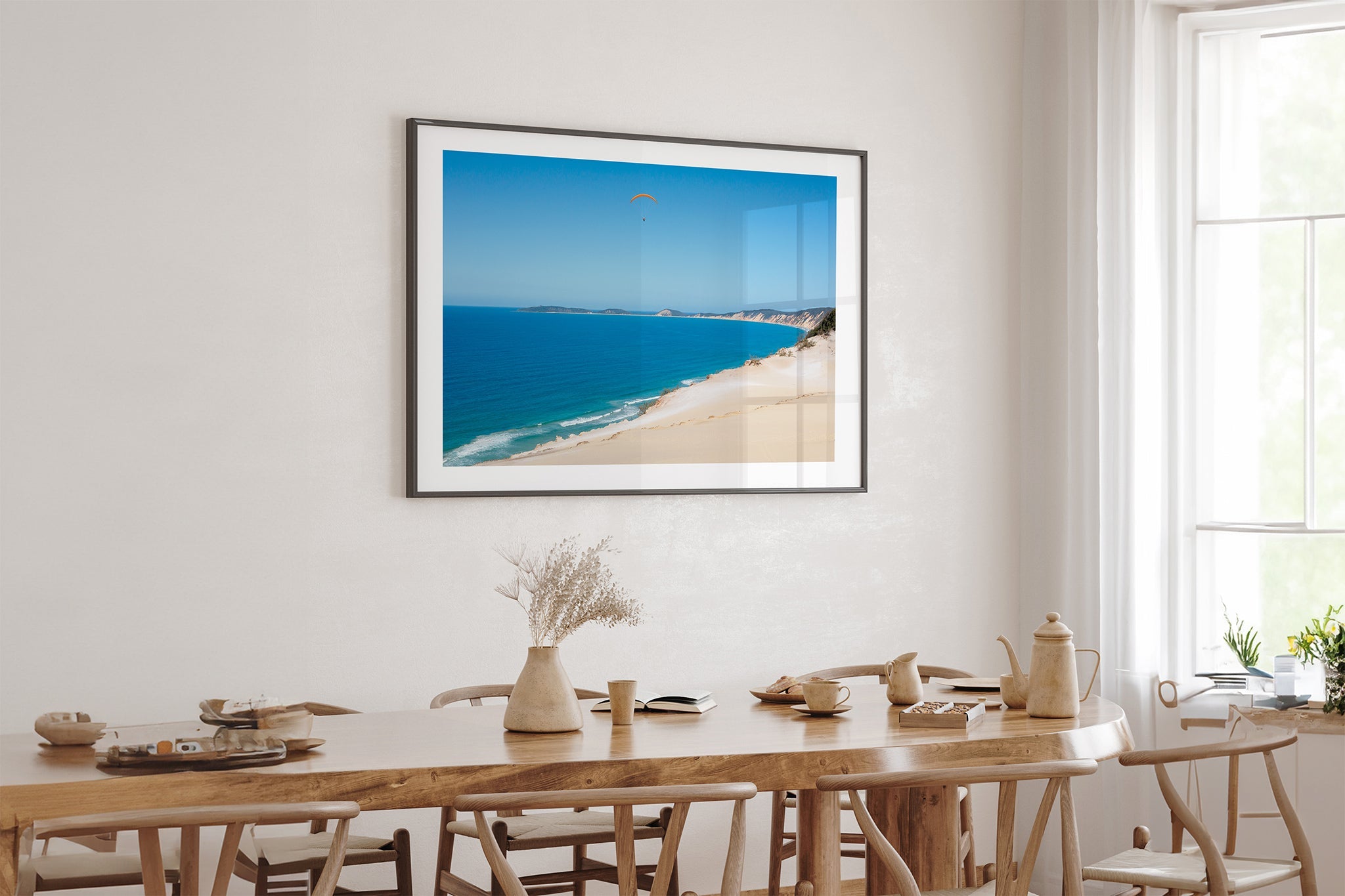 Rainbow Beach paraglider print shown framed in black above an oak dining table.