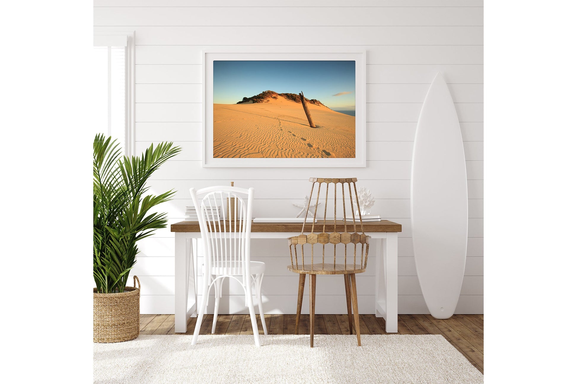 Rainbow Beach dune print shown framed in white above a desk beside a surfboard.