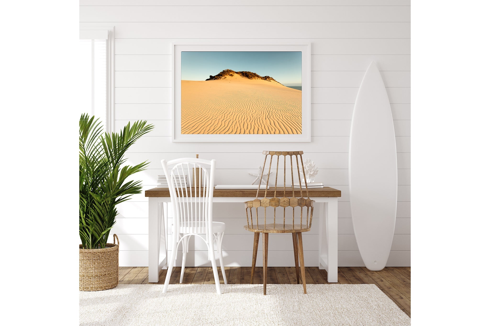 Rainbow Beach golden dunes print shown framed in white above a desk beside a surfboard.