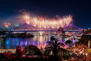 Brisbane's Story Bridge during Riverfire, dense fireworks bursting above it, city skyline and crowds visible, a wall print.