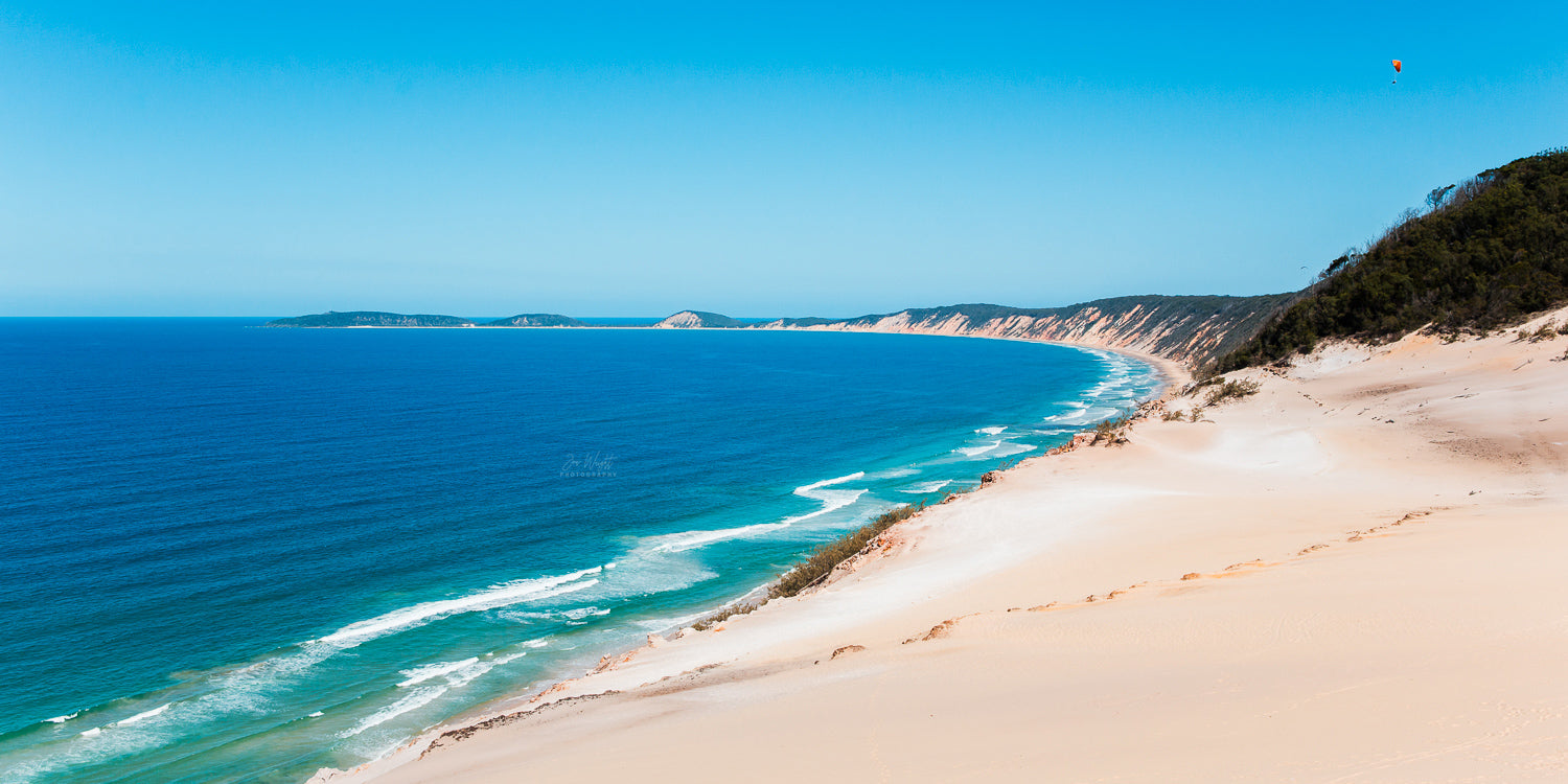 Wide view from the Carlo Sand Blow at Rainbow Beach, deep blue ocean beside pale dunes and coloured cliffs, a panoramic wall print.
