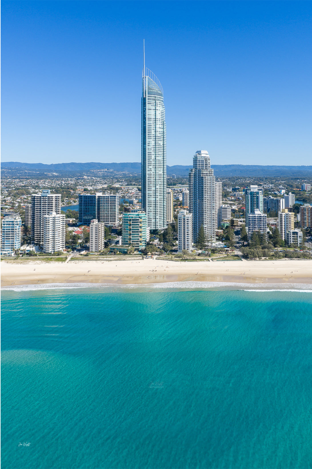Aerial view of Q1 Tower rising above the Surfers Paradise skyline, with pale sand and turquoise water below.
