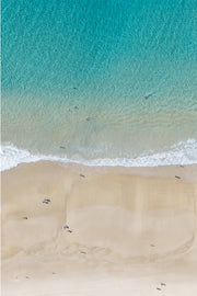 Aerial view of rippled turquoise shallows meeting pale sand, with a few swimmers scattered through the water.