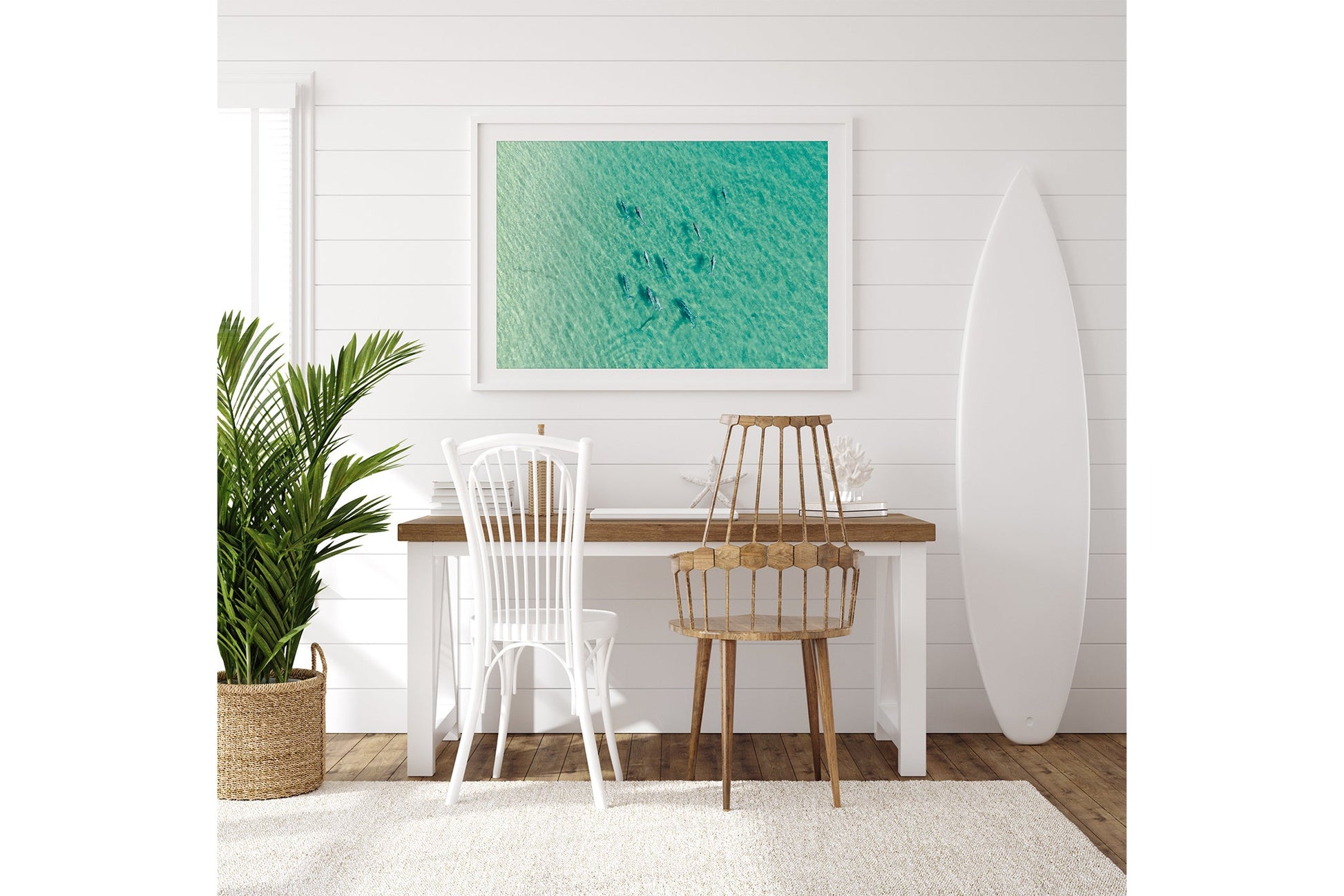 Moreton Bay dolphin pod print shown framed in white beside a surfboard in a coastal room.