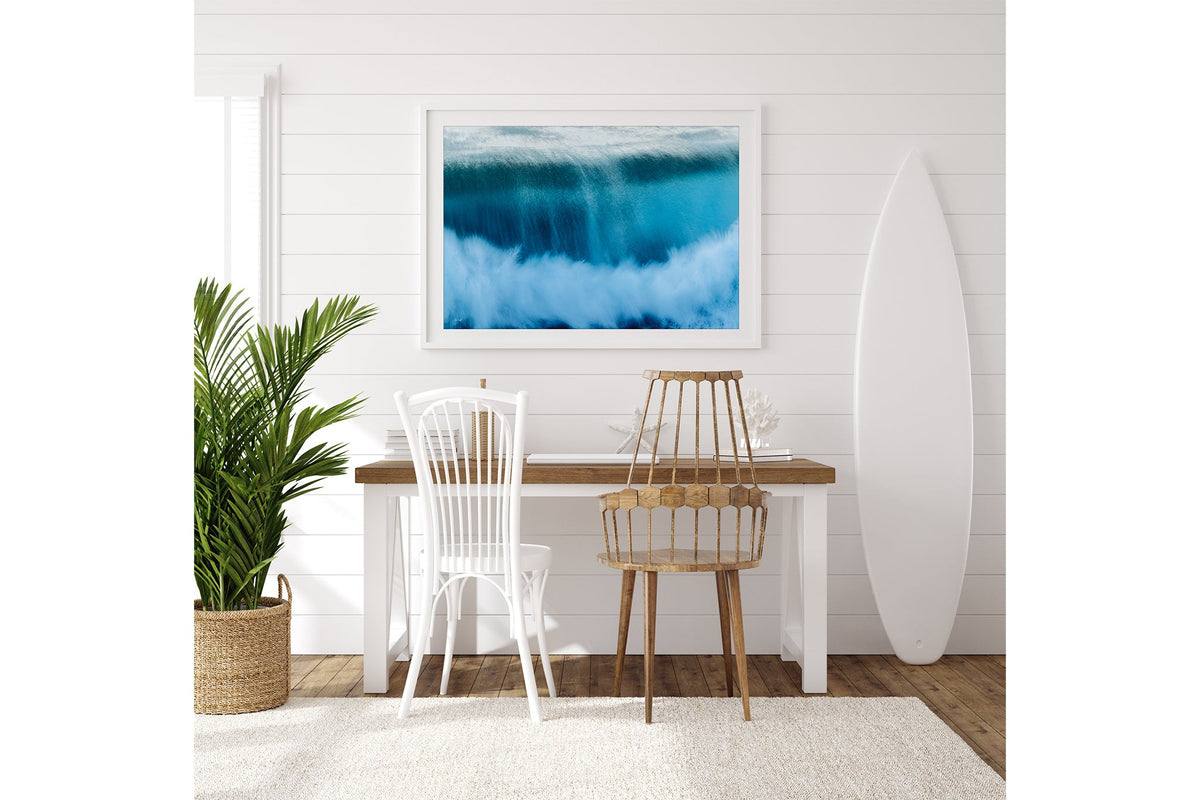 Deep Impact wave print shown framed in white on a white shiplap wall beside a desk.