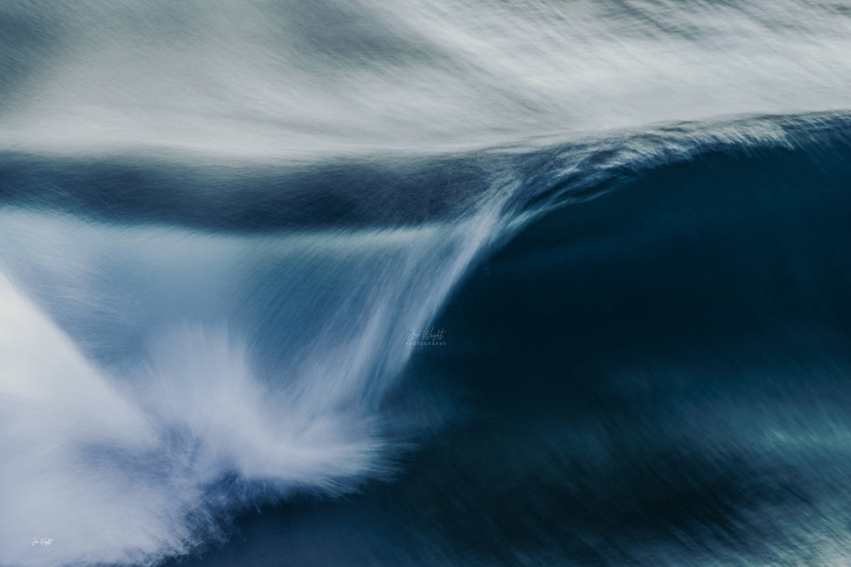 An abstract navy blue wave curling at right with white spray streaking across the frame in long motion blur.