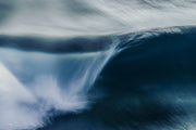 An abstract navy blue wave curling at right with white spray streaking across the frame in long motion blur.