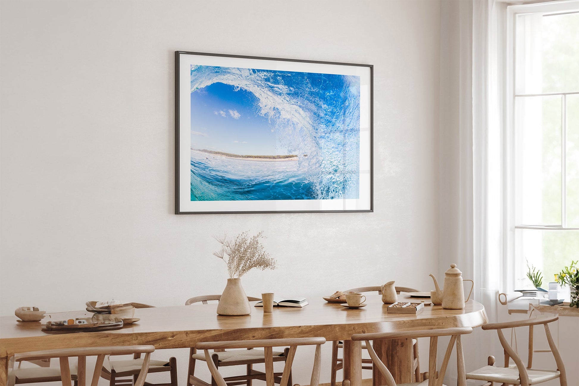 Blue barrel wave print shown framed in black, hung above a light oak dining table in a bright neutral room.