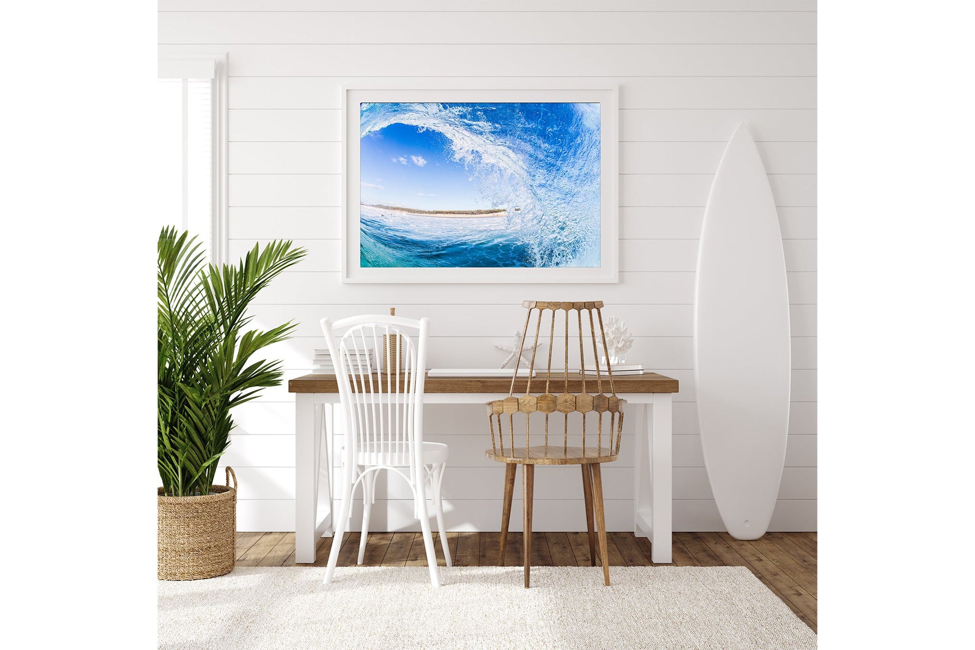 Blue barrel wave print shown framed in white, hung above a coastal style desk with a surfboard standing alongside.