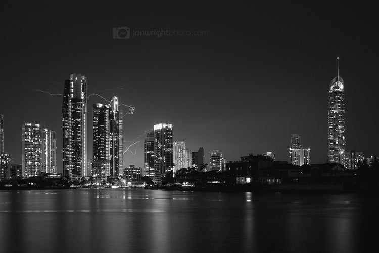 Black and white city skyline at night with tall buildings and a body of water.