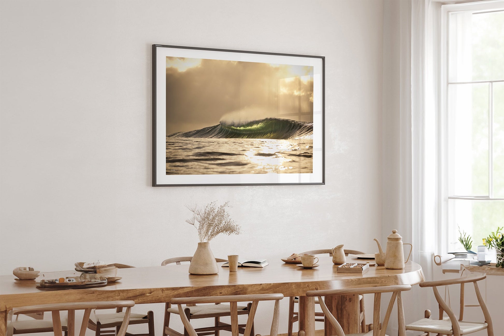 Golden sunset wave print shown framed in black, hung above a light oak dining table in a bright neutral room.