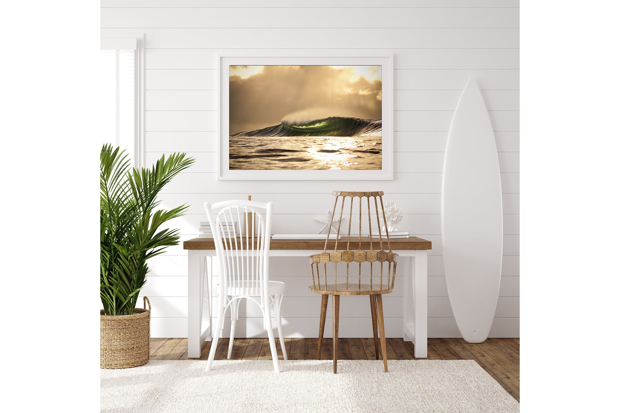 Golden sunset wave print shown framed in white, hung above a coastal style desk with a surfboard standing alongside.