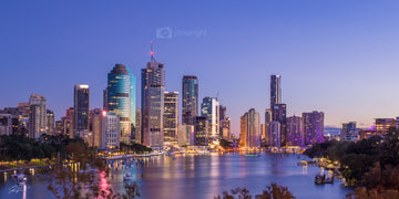 Brisbane's skyline at dusk from Kangaroo Point cliffs, city lights lit, reflective river water under a purple sky, a wall print.